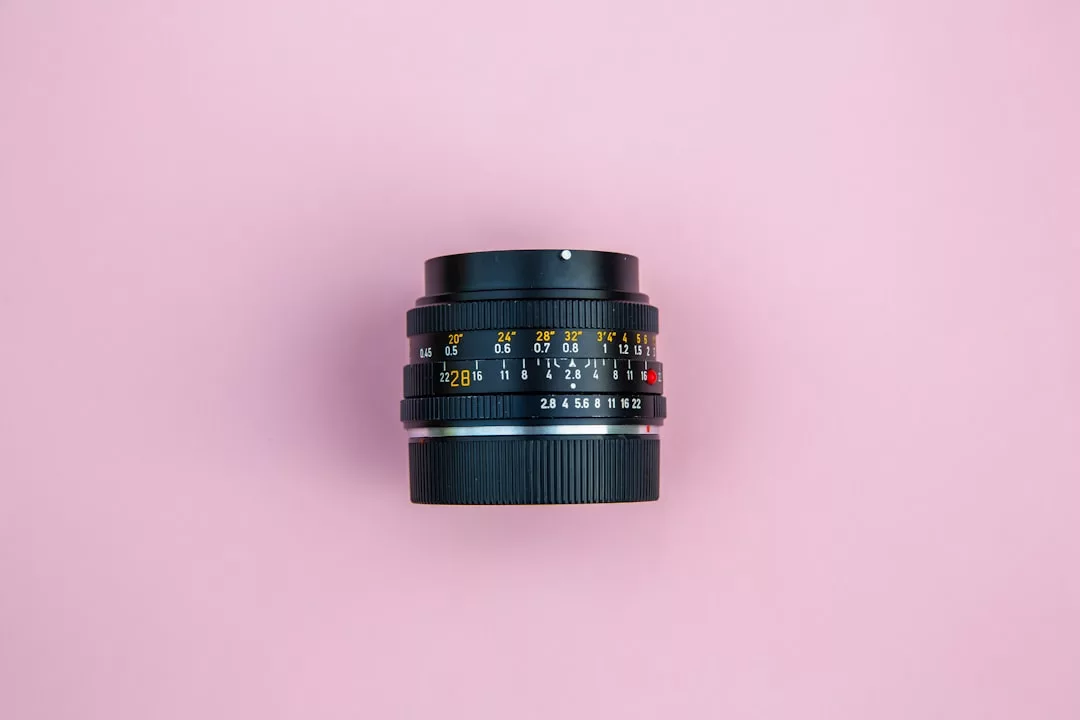 A black camera lens with yellow and white markings, perfect for real estate photography, is placed on a pink background.