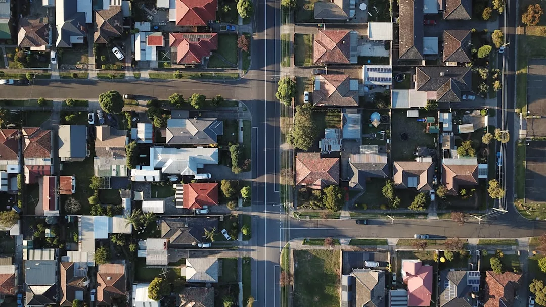 Aerial view of a suburban neighborhood, showcasing real estate with houses, roads, trees, and parked cars arranged in a neat grid pattern.