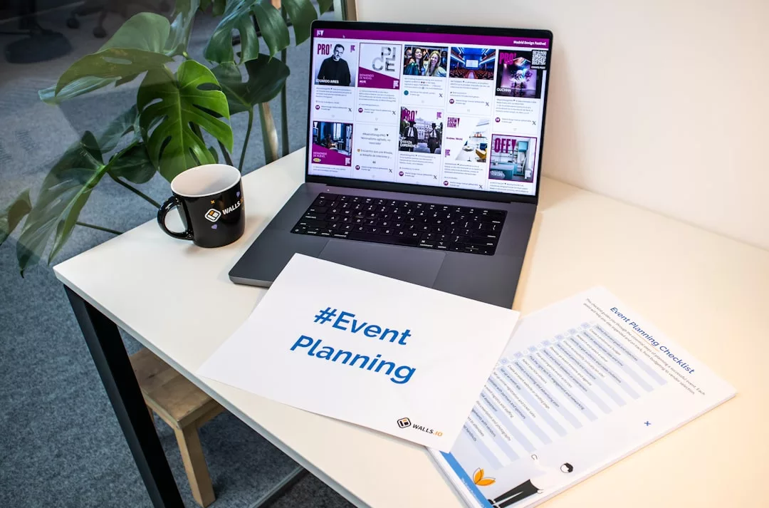 A laptop displaying an event website, a coffee mug, a plant, a Real Estate brochure, an #Event Planning sign, and a printed checklist sit on a white desk in an office setting.