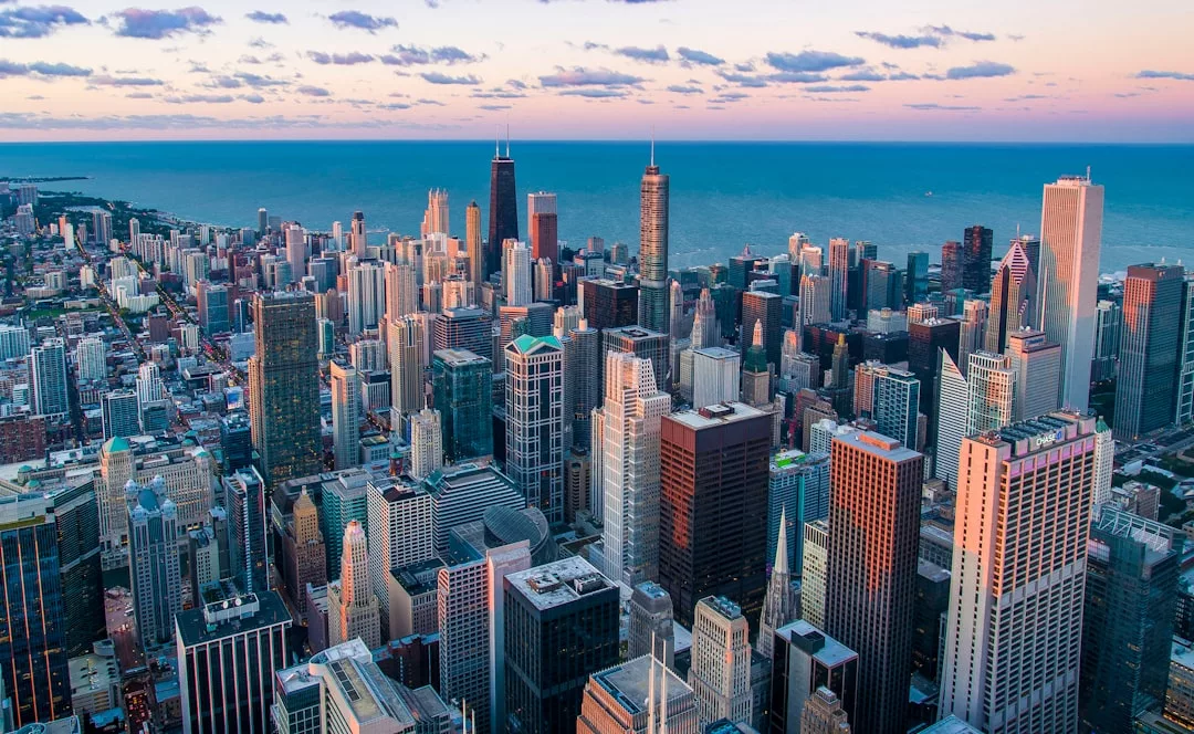 Aerial view of a city skyline with tall buildings, prime real estate, Lake Michigan in the background, and a pastel sky at sunset.