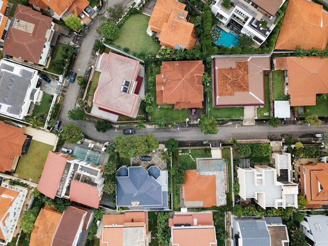 Aerial view of a suburban neighborhood showcasing prime real estate, with houses featuring red and gray roofs, green lawns, trees, and a curved road winding through the area.
