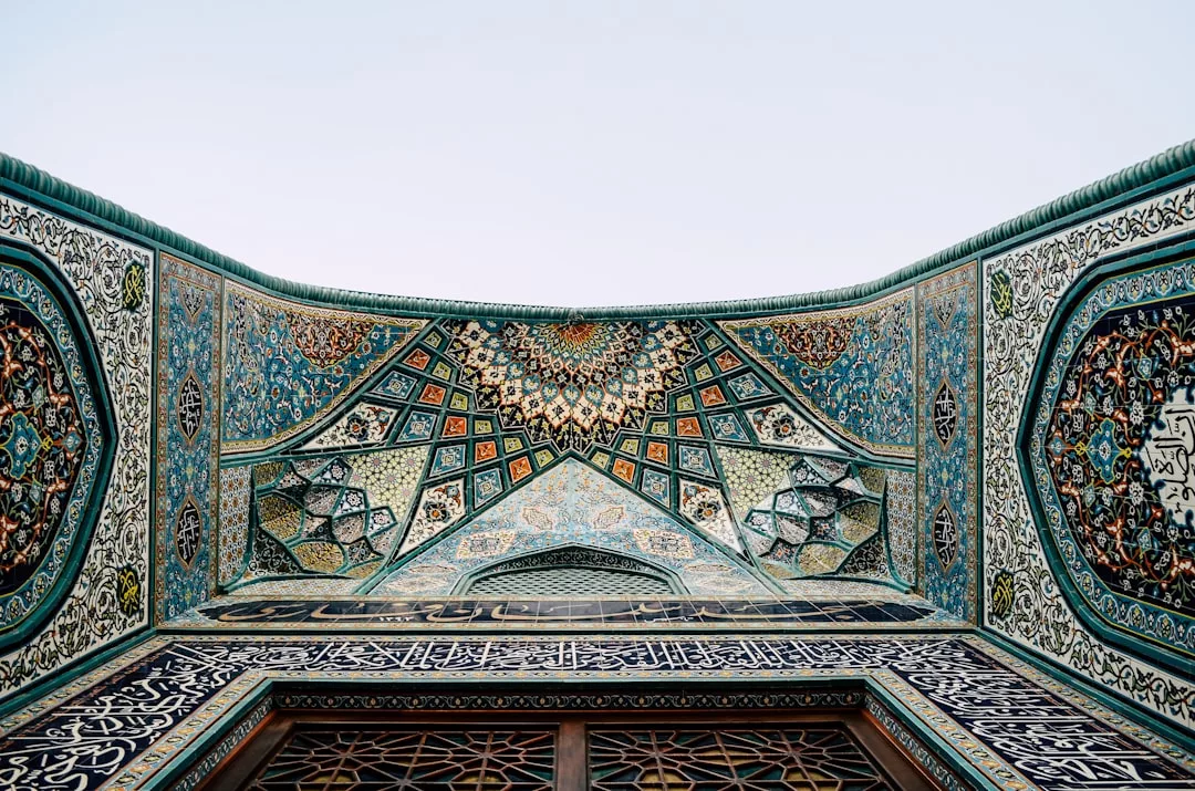 Ornate mosaic ceiling and walls of an Islamic building, featuring geometric patterns and Arabic calligraphy in blue, green, orange, and white—an exquisite example of architecture ideal for distinguished real estate.