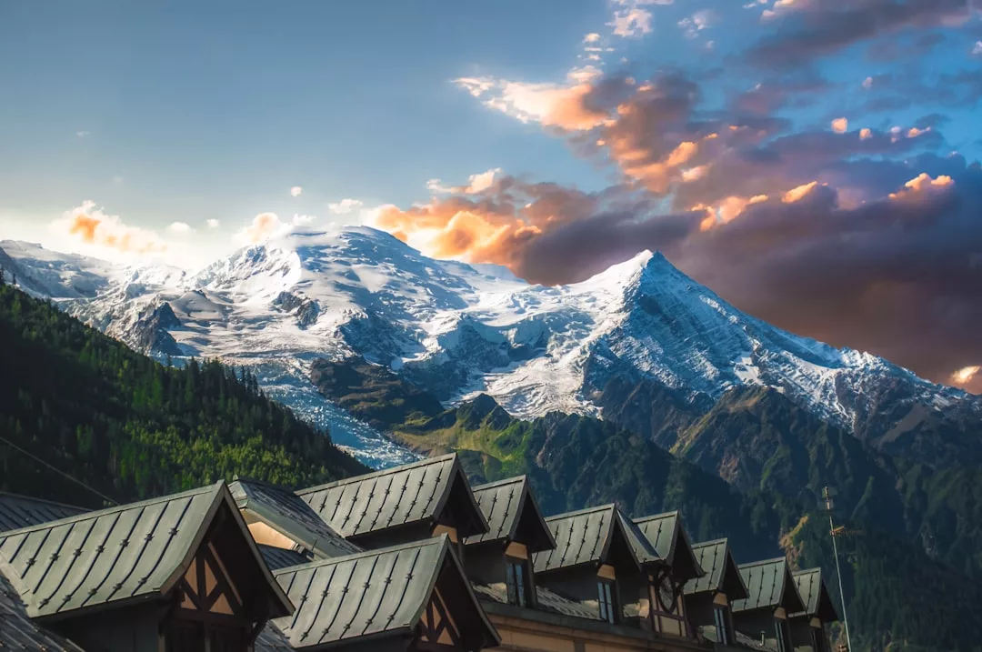 Snow-capped mountains under a dramatic sunset sky, with rooftops of several real estate buildings in the foreground.