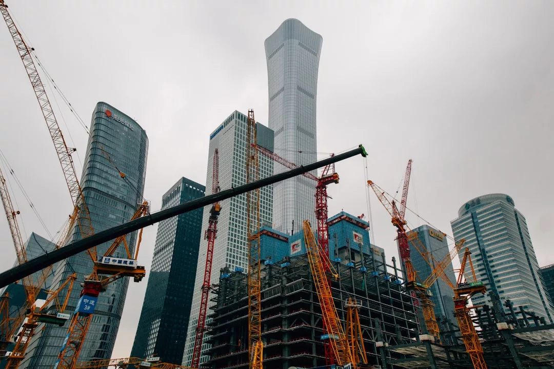A cityscape featuring modern skyscrapers under construction, with multiple yellow cranes and steel frameworks visible against an overcast sky, highlights the dynamic growth of urban real estate.