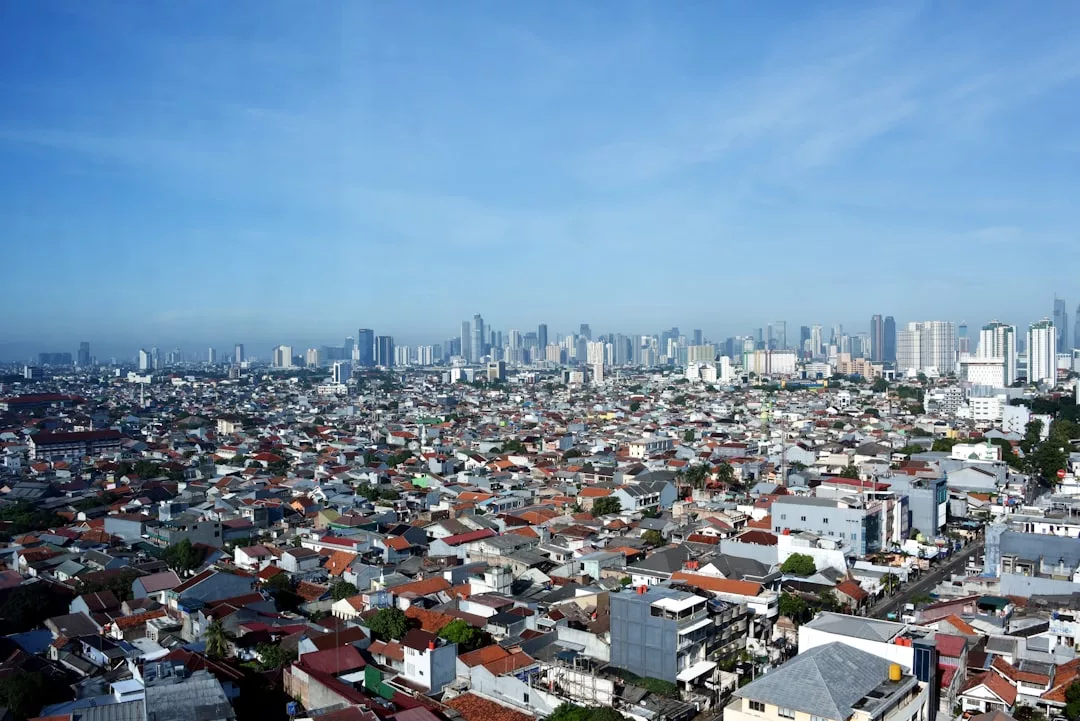 A wide view of a densely populated city showcases low-rise residential buildings in the foreground and modern high-rise real estate developments in the background under a clear blue sky.