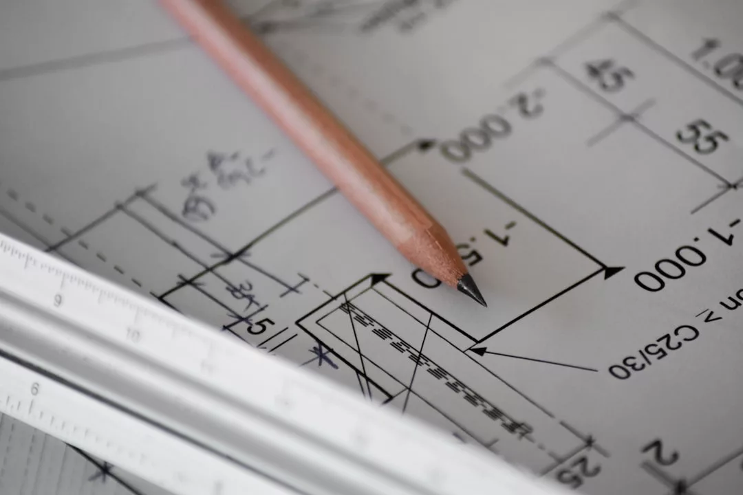 A close-up of a pencil and a ruler resting on technical architectural drawings with precise measurements and lines, capturing the precision behind every real estate project.