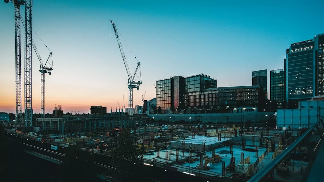 A construction site with cranes and building materials in the foreground, surrounded by modern office buildings at sunset—capturing the dynamic growth of real estate in the city.