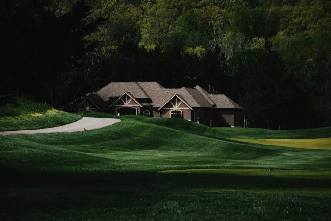 A beautiful real estate gem, this house with multiple gables sits behind a green lawn and a winding path, bordered by dense trees in the background.
