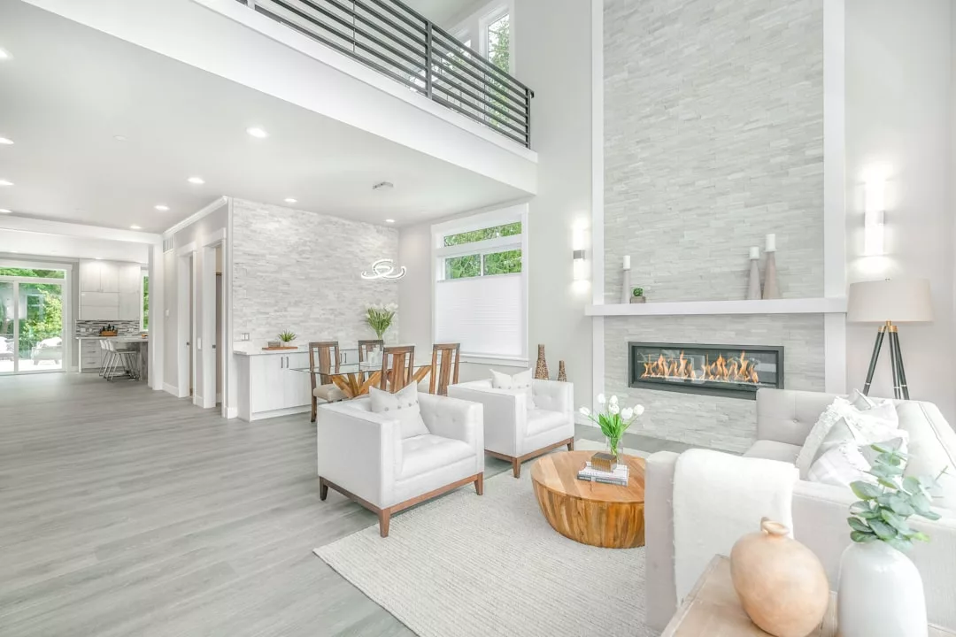Modern living room with white walls, light wood flooring, a stone fireplace, and contemporary furniture—perfect for showcasing your Real Estate. Natural light fills the open space, with a dining area visible in the background.