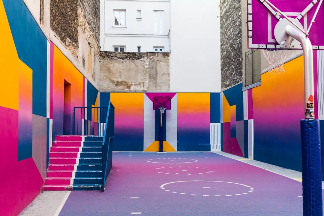 A small urban basketball court with vibrant, colorful walls and floor featuring geometric patterns in pink, orange, blue, and yellow—one of the standout amenities found in family-friendly Stockholm neighborhoods.