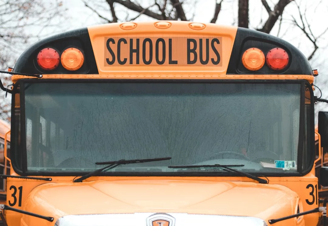 Close-up view of the front of a yellow school bus with "SCHOOL BUS" sign displayed above the windshield, set against a backdrop of trees—an everyday scene near local real estate developments.