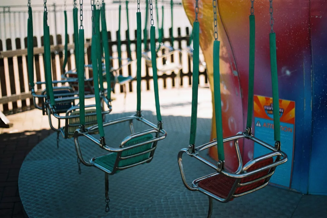 Empty metal swing ride seats with green straps hang from chains near a colorful wall and wooden fence in an outdoor amusement park—capturing the playful spirit of Oslo’s family-friendly neighborhoods and ideal home atmosphere.