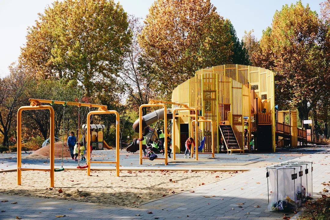 Children play on swings and climbing structures in a modern outdoor playground, surrounded by tall autumn trees and scattered leaves—perfect for families seeking an ideal home in Stockholm.