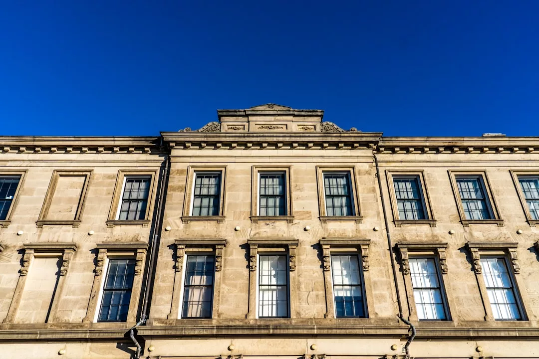 A beige stone real estate building with tall rectangular windows and decorative architectural details stands against a clear blue sky.