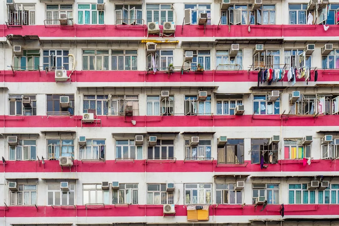 Facade of a real estate apartment building featuring red horizontal stripes, rows of windows, balconies with air conditioners, and laundry hanging outside.
