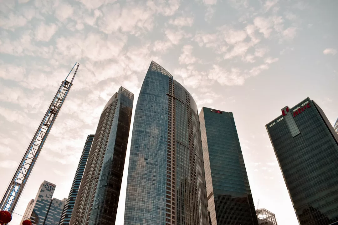 Several modern high-rise office buildings and a construction crane rise against a partly cloudy sky, showcasing the vibrant Real Estate development, photographed from a low angle.