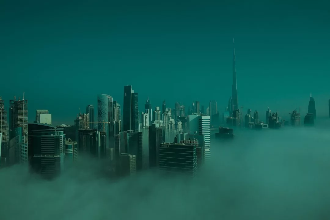 A city skyline with tall skyscrapers rises above dense fog under a teal-colored sky, showcasing the impressive allure of urban real estate.