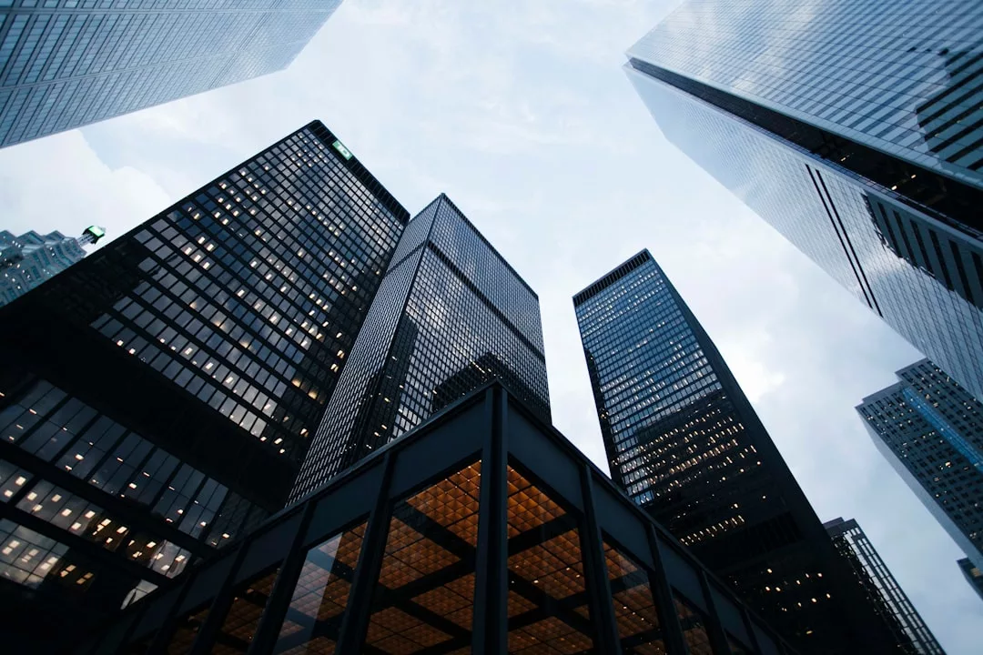 Tall modern skyscrapers viewed from below against a cloudy sky, their glass and steel exteriors reflecting light—a striking vision of urban real estate.