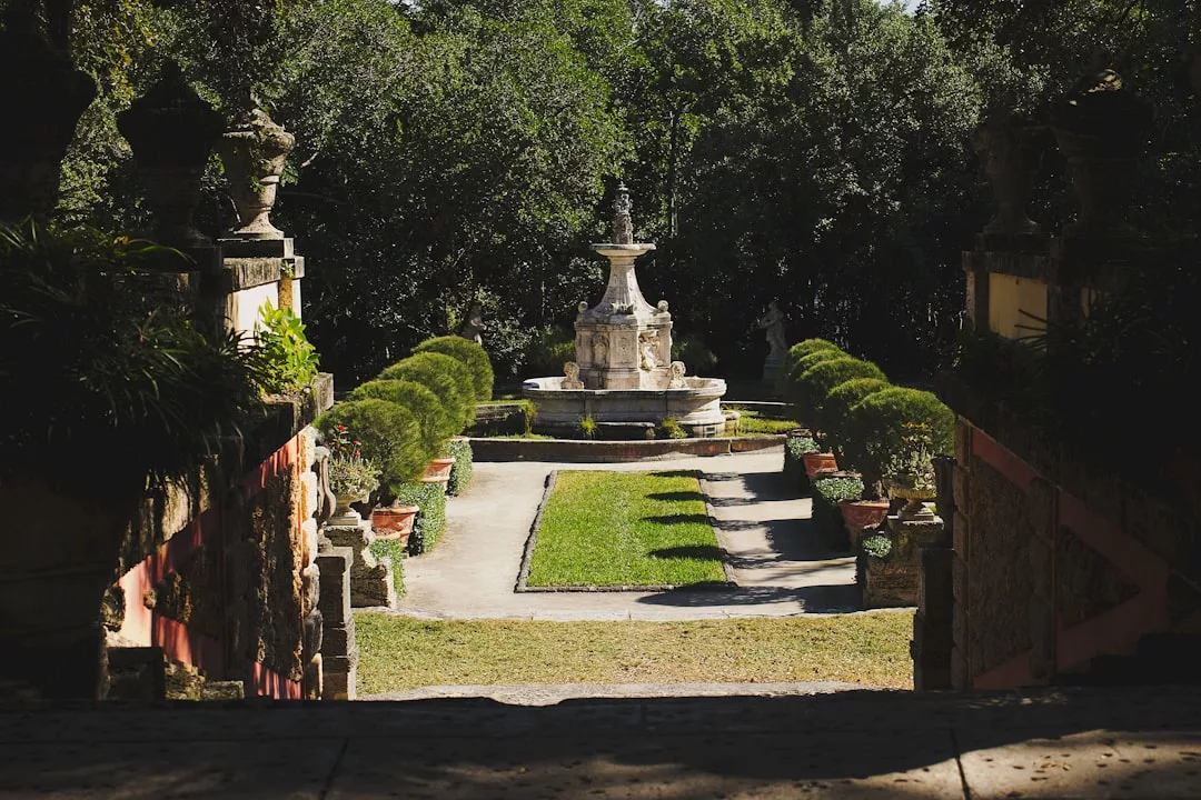 Stone staircase overlooks a formal garden with trimmed hedges and a central stone fountain, making this Real Estate property stand out, surrounded by trees and decorative urns.