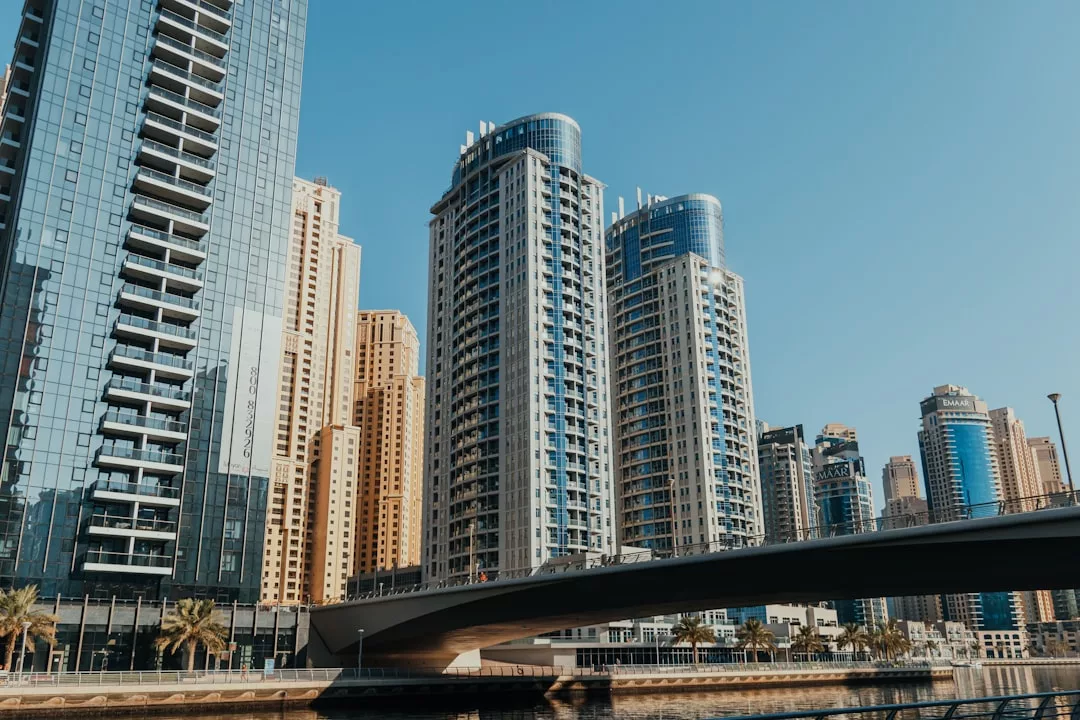 Modern high-rise buildings with glass facades, exemplifying prime real estate, stand under a clear blue sky next to a bridge in an urban cityscape.