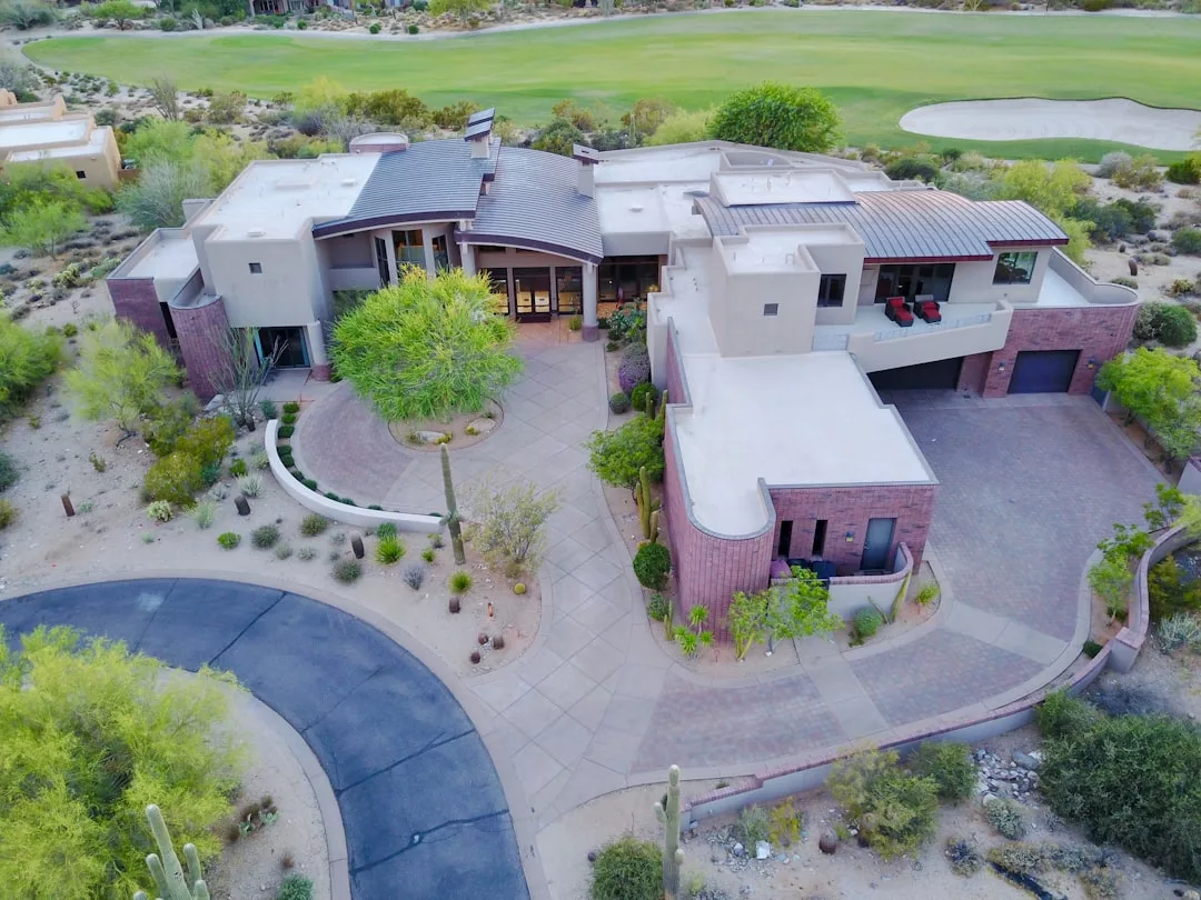 A modern, multi-level real estate gem with a curved driveway, surrounded by desert landscaping and located next to a golf course.