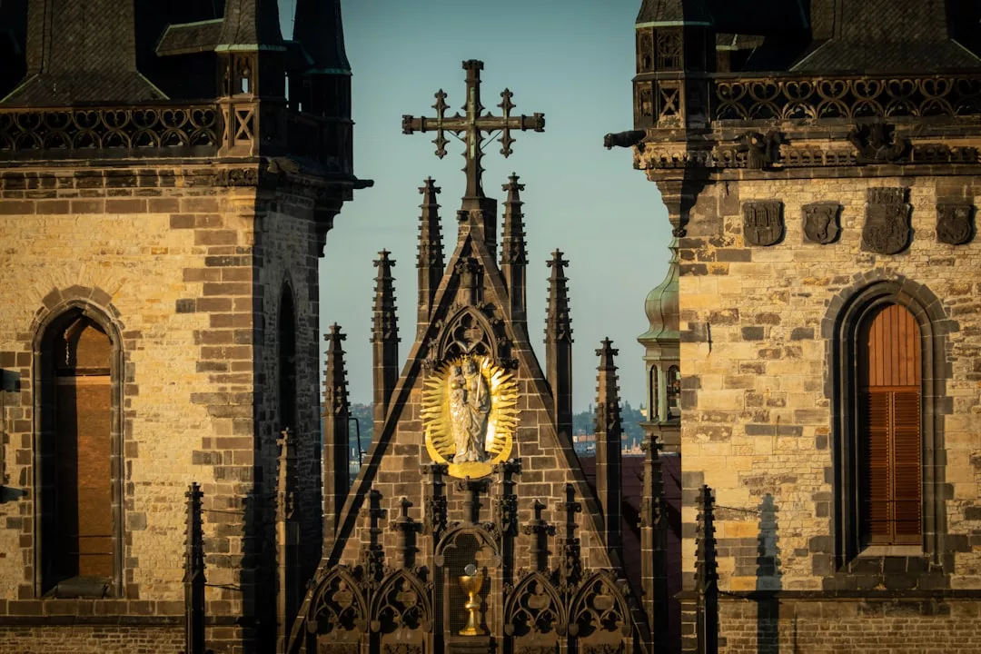 Close-up view of a Gothic cathedral facade with a large ornate cross, a golden halo decoration, and two stone towers featuring arched windows—an architectural gem that stands out in real estate listings.