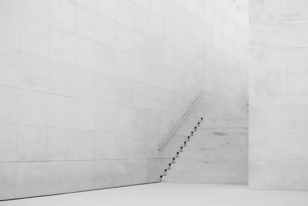 Minimalist scene of white concrete stairs with a metal handrail, adjacent to large tiled walls, in a modern architectural space inspired by Copenhagen’s urban development in Ørestad.