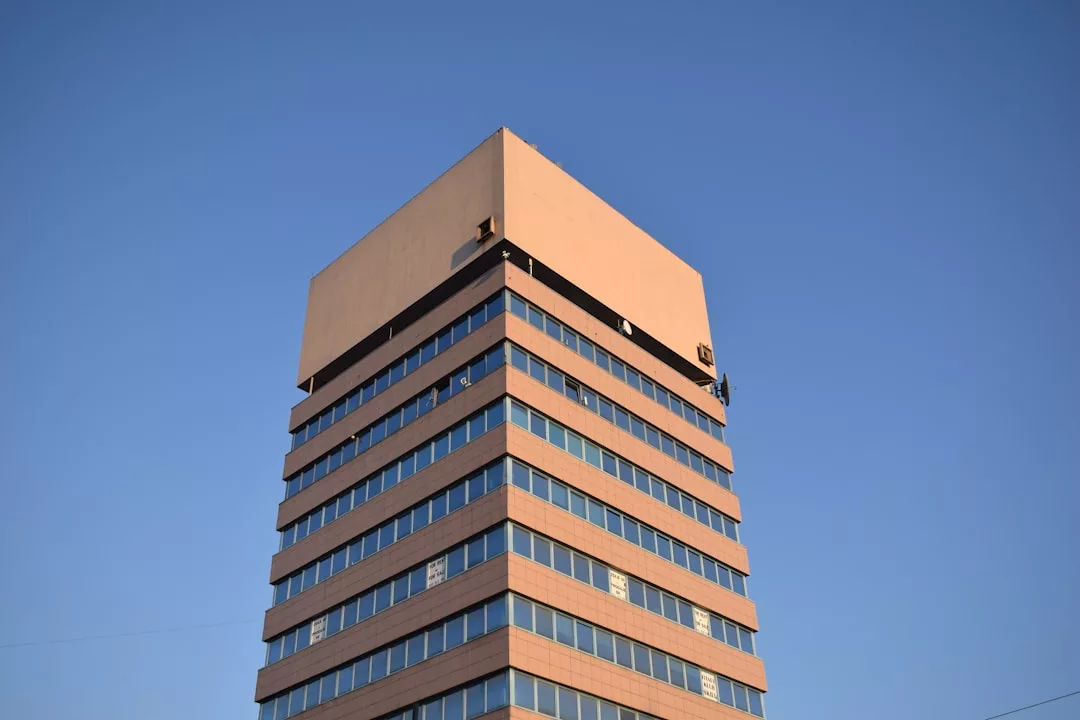A multi-story office building, ideal for real estate investment, features a large square structure on top, set against a clear blue sky.