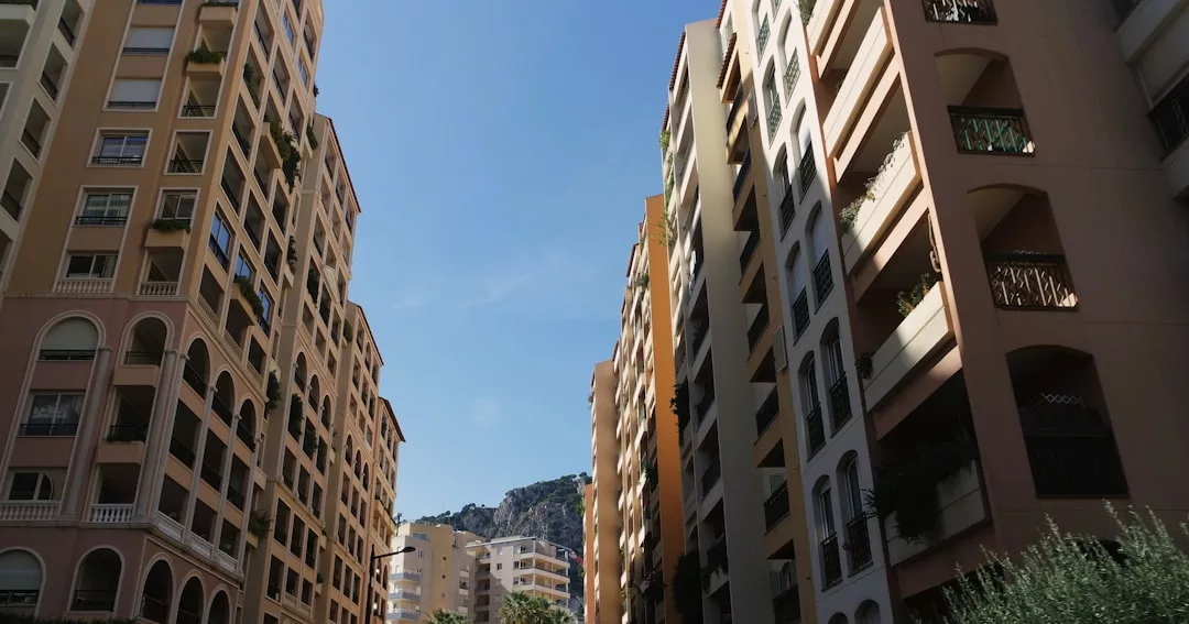 Tall apartment buildings, ideal for real estate opportunities, line both sides of a narrow street under a clear blue sky, with distant hills visible in the background.