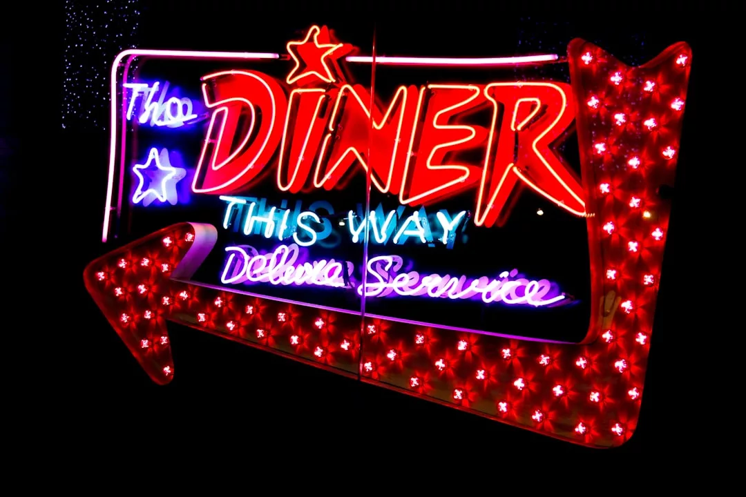 Neon sign with red and purple lights reads “The Diner This Way Deluxe Service,” featuring a large red arrow pointing left—an eye-catching piece, perfect for adding retro flair to any real estate or commercial space.