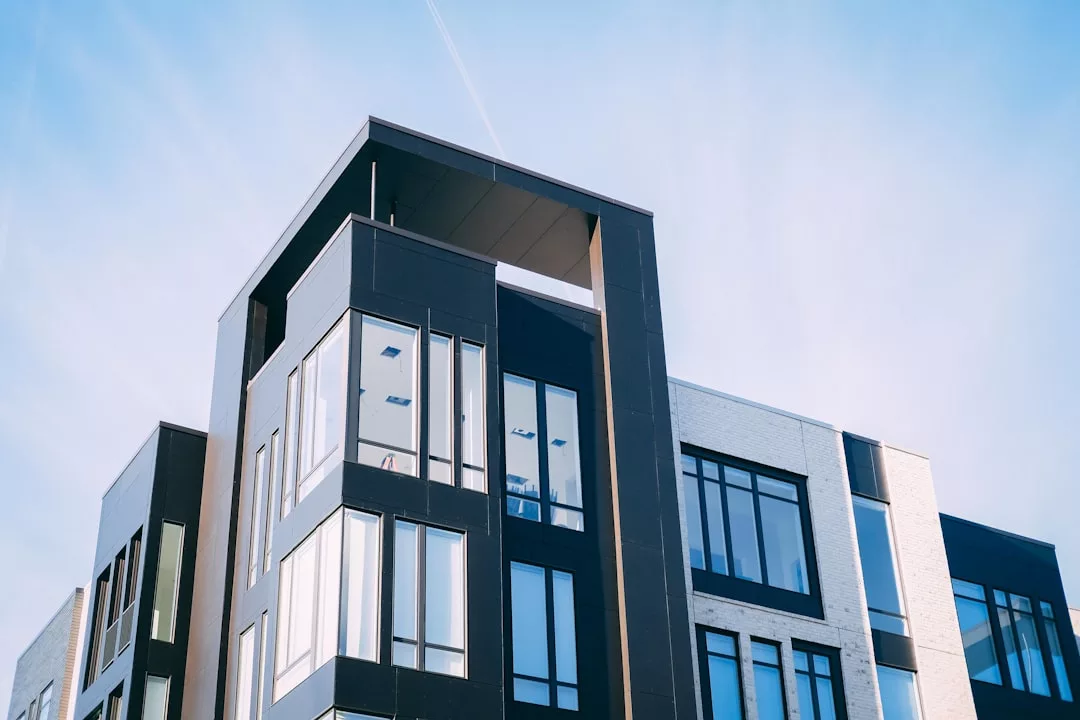 Modern real estate apartment building with large windows and geometric architectural design, photographed from a low angle against a clear blue sky.