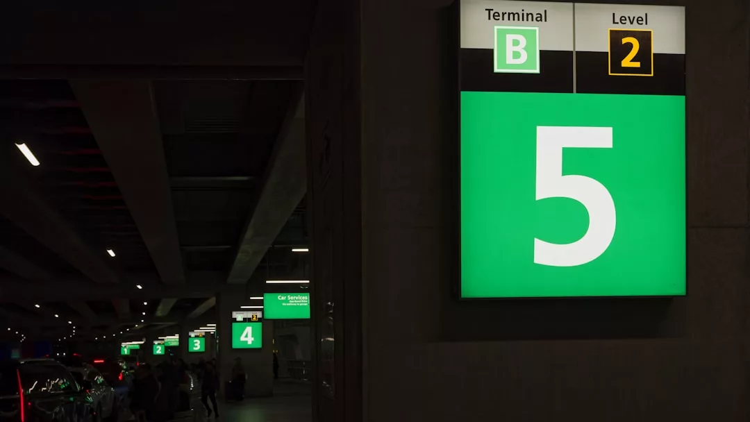 A brightly lit green parking sign shows "5" at Terminal B, Level 2 in a parking garage—a convenient detail for real estate professionals highlighting property access, with similar numbered signs visible in the background.