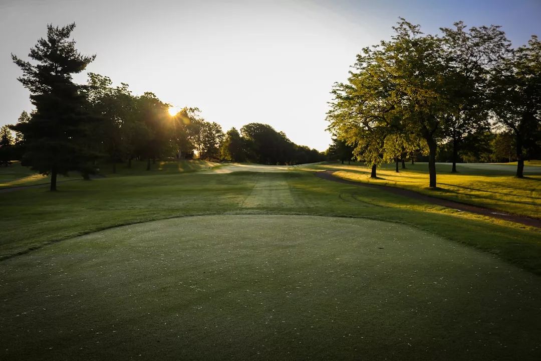 Sunrise over a golf course with a view of the green, trees lining the fairway, and sunlight filtering through the branches—an inviting scene for premium real estate nestled in natural beauty.