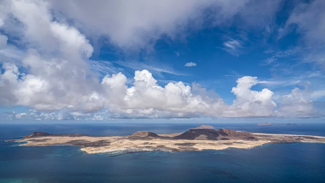 Aerial view of an arid island with rocky hills, ideal for unique real estate opportunities, surrounded by blue ocean under a partly cloudy sky.