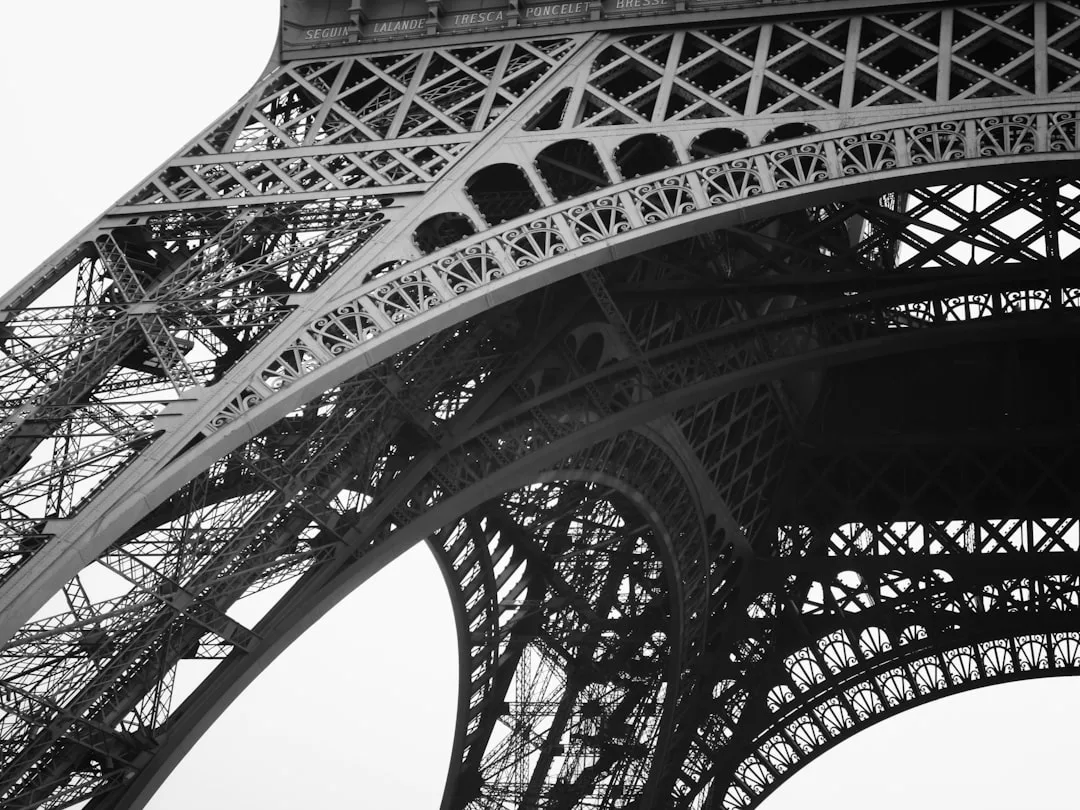 Black and white photo showing a close-up view of the intricate iron framework at the base of the Eiffel Tower, capturing architectural details that inspire modern real estate design.