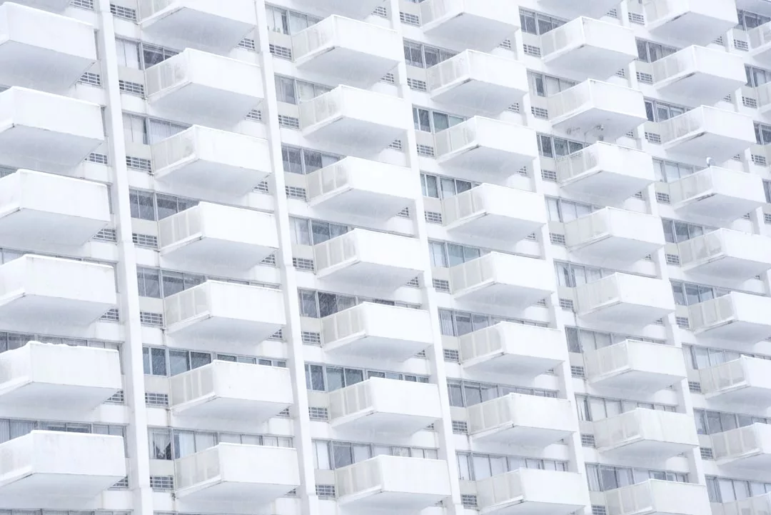 A white high-rise real estate property with repeating rows of balconies and windows, creating a striking geometric, grid-like pattern.