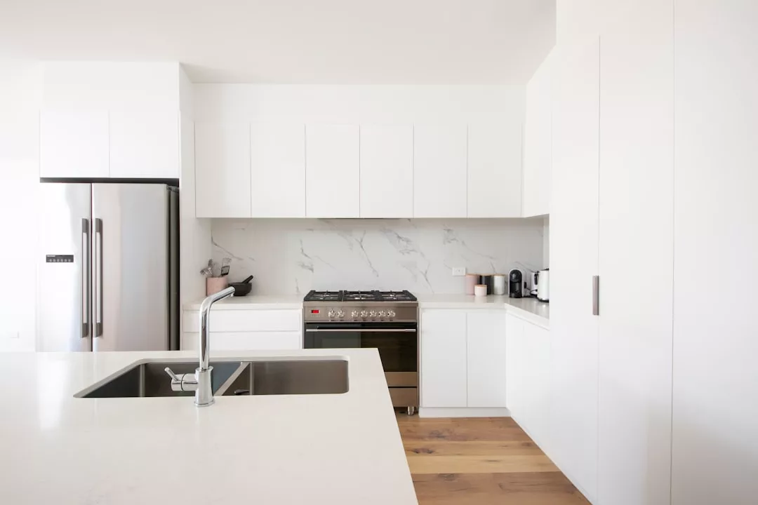 Modern kitchen with white cabinets, stainless steel refrigerator, gas stove, and marble backsplash—perfect for real estate showings. Island countertop features a sink with faucet and space for small appliances.