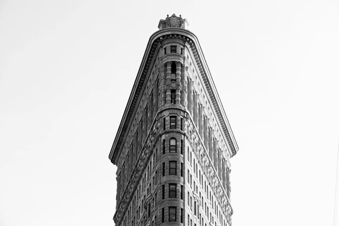 Black and white photo of the Flatiron Building in New York City, an iconic marvel of early real estate, viewed from the narrow, pointed end looking up toward the sky.