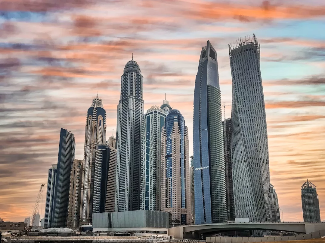 A cluster of modern skyscrapers in Dubai stands against a colorful sunset sky, showcasing architectural variety and reflective glass facades that highlight the city's thriving real estate landscape.