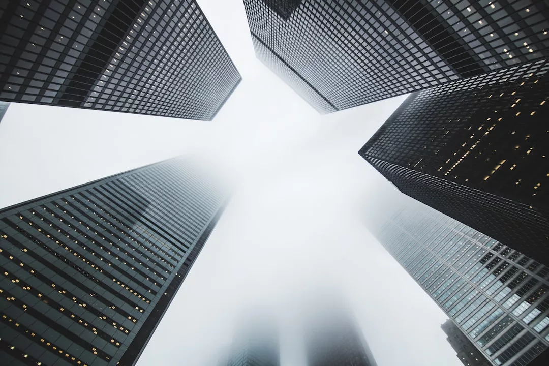 Towering skyscrapers, symbols of modern real estate, rise into the fog with their tops disappearing into the cloudy sky.