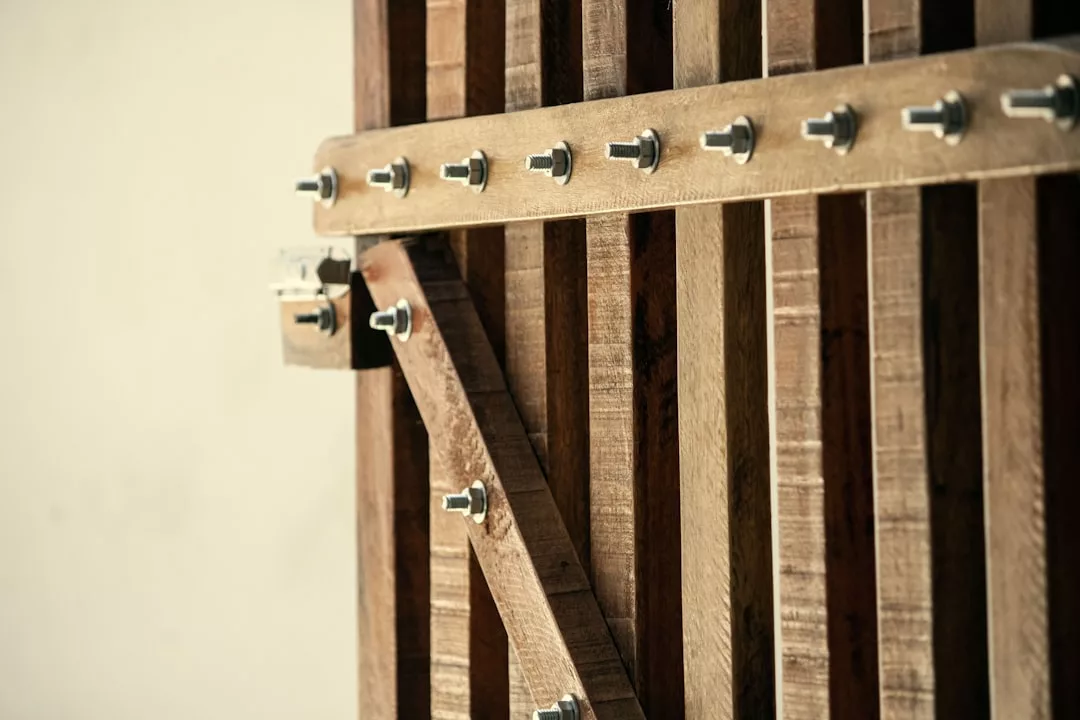 Close-up of a wooden gate with metal bolts and a padlock on the left side, set against a plain, light-colored background—a secure feature often seen in quality real estate.