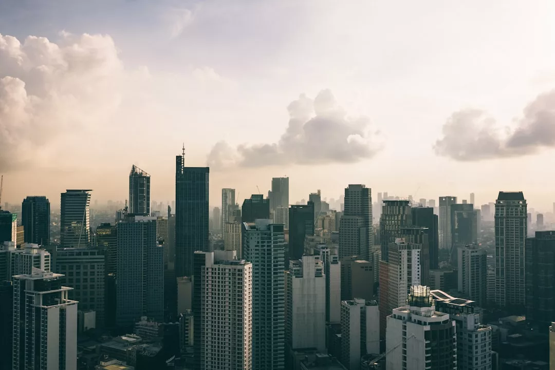 A city skyline with numerous high-rise buildings, showcasing the vibrancy of urban real estate, under a partly cloudy sky during daylight.