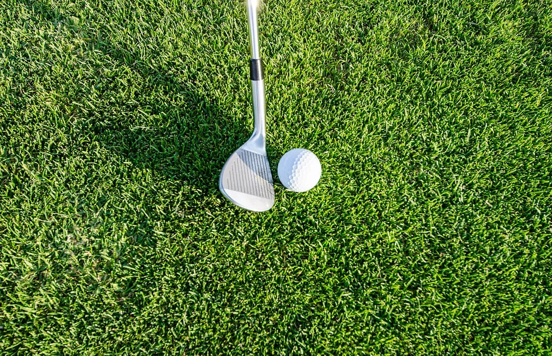A golf club positioned next to a golf ball on green grass, offering a glimpse of luxury living often found in exclusive real estate communities.