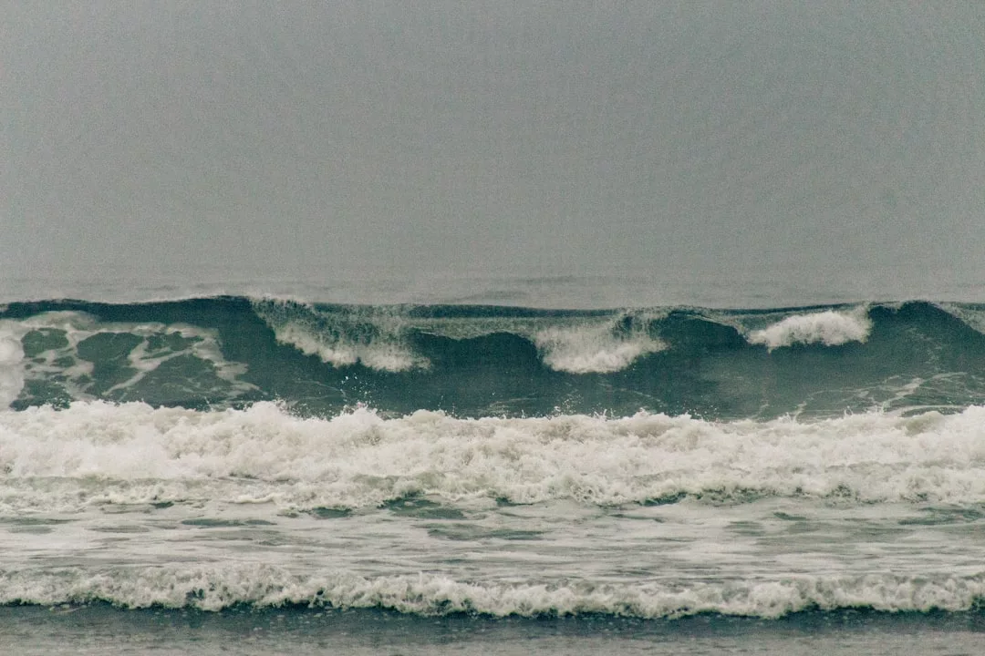 Gray, overcast sky above rough ocean waves breaking and rolling toward the shore—an inspiring view that highlights the natural beauty found in sought-after coastal real estate.