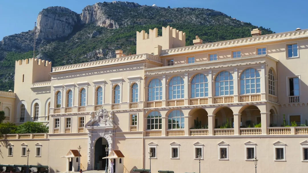 Historic cream-colored palace with arched windows and crenellated towers, set against a rocky, tree-covered mountain under a clear blue sky—a breathtaking real estate gem.
