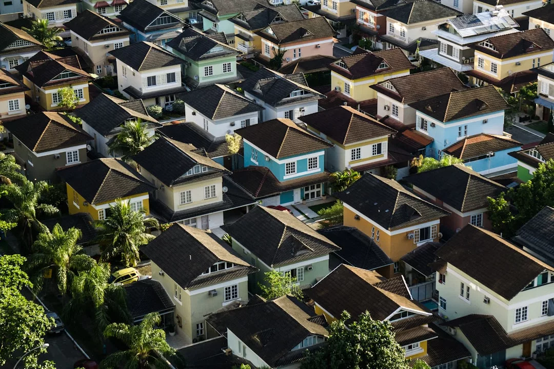 Aerial view of a suburban neighborhood highlights rows of colorful, two-story homes surrounded by trees and greenery—a picturesque real estate opportunity.