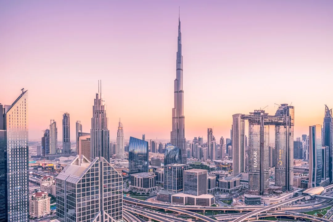 A cityscape of modern skyscrapers at sunset, featuring a tall, central tower and highways in the foreground under a pastel sky—a stunning vista symbolizing vibrant urban life and real estate opportunity.