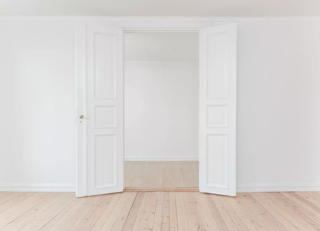 A pair of white double doors open into an empty, bright room with white walls and light wood flooring—an inviting space perfect for your next real estate opportunity.