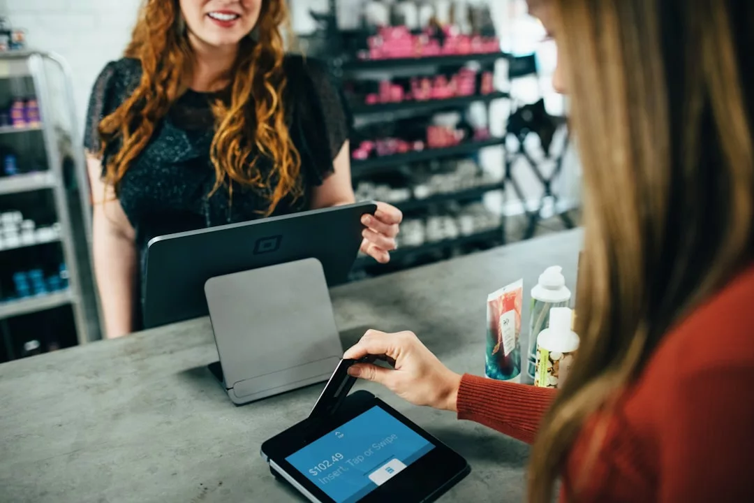A customer uses a credit card to pay at a touchscreen terminal while a cashier stands behind the counter in a retail store, highlighting seamless transactions that are equally essential in Real Estate settings.