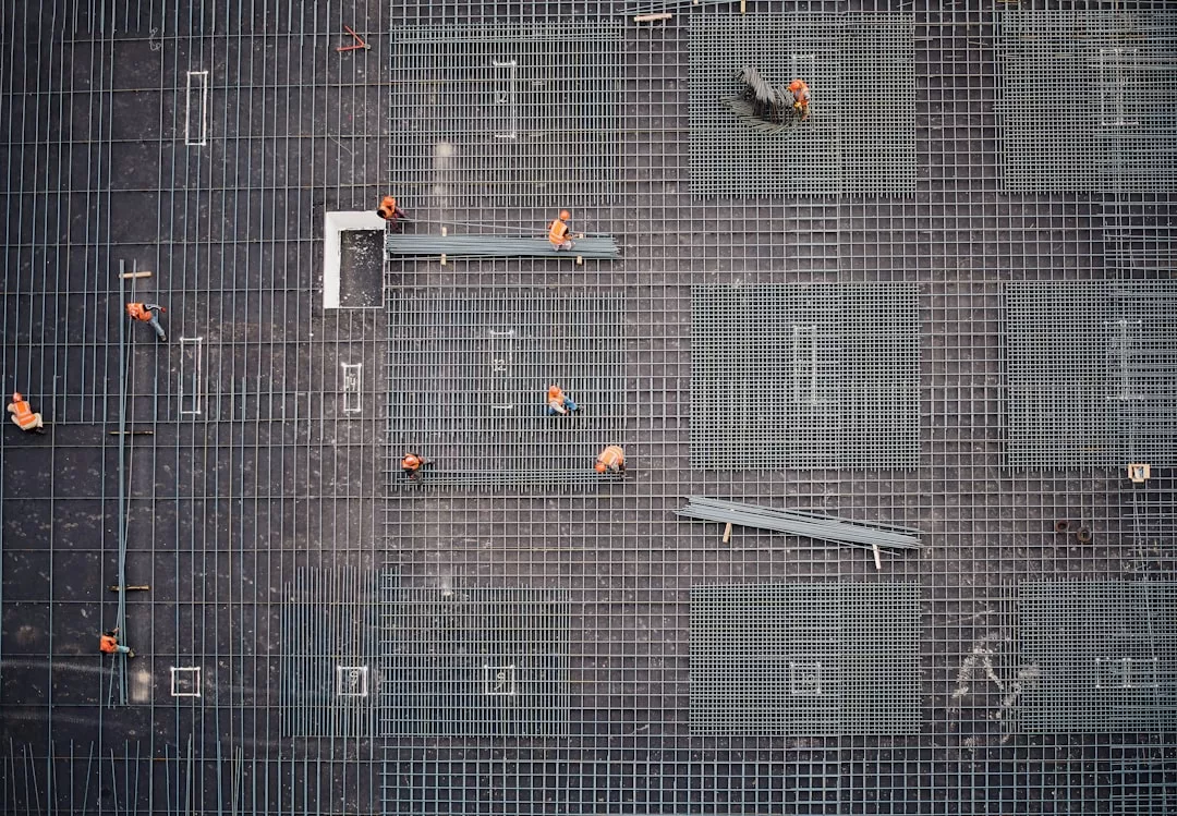 Aerial view of construction workers in orange helmets standing and walking on a grid of steel rebar at a real estate building site.